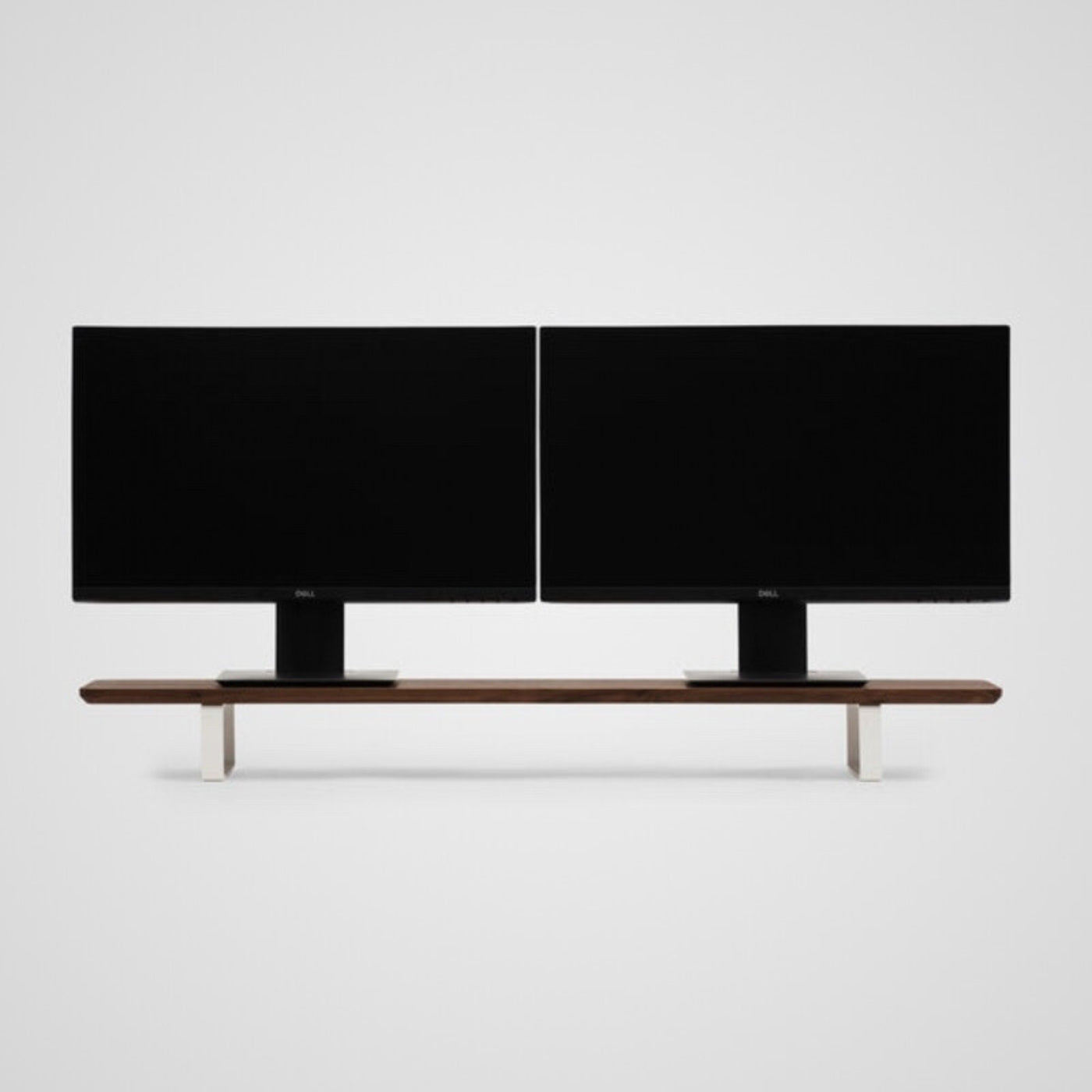 Dual Dell monitors on walnut wood office desk riser with white metal legs, minimalist workspace