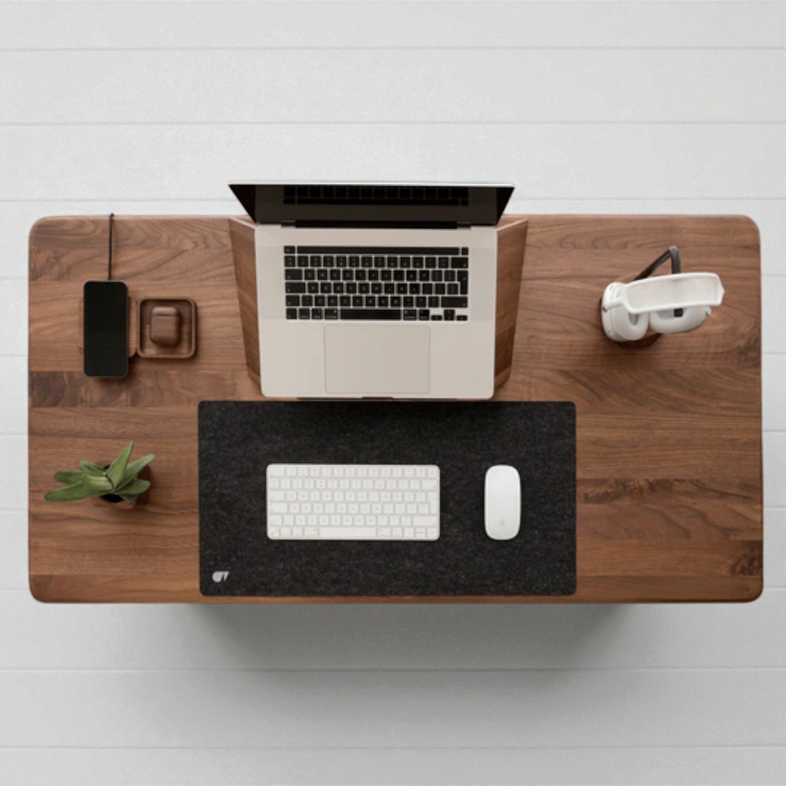 Walnut standing desk with laptop, white keyboard, mouse, plant, and headset, modern workspace