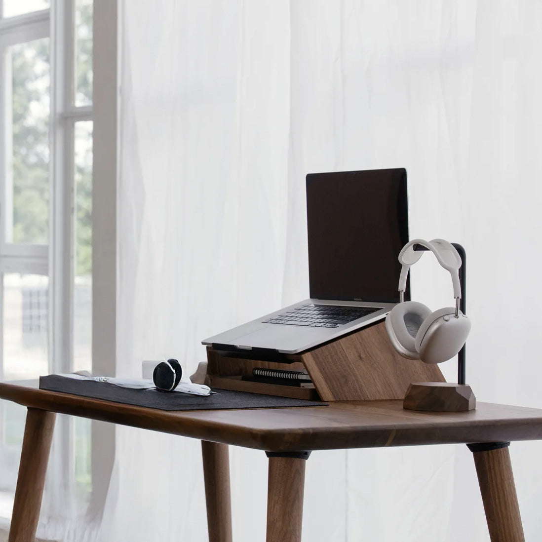 Wooden laptop stand with laptop and white headphones on a wooden desk in a modern office setting