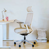 Beige pelicanwork ergonomic office chair with headrest beside white desk in modern workspace